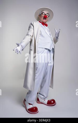 Ein älterer Clown mit weißem Mantel und Hut. Der Mann trägt große rote Clownstiefel aus Lackleder Stockfoto