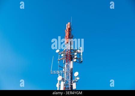 Mobilfunk-Kommunikationsturm mit Antennen und Mikrowellensendern vor klarem blauem Himmel, moderne Telekommunikationsinfrastruktur Stockfoto