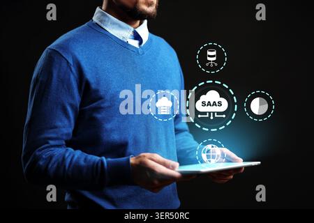 Man hält ein Tablet mit SaaS-Grafik in dunkler Umgebung und betrachtet dabei Clouds und Datensymbole Stockfoto