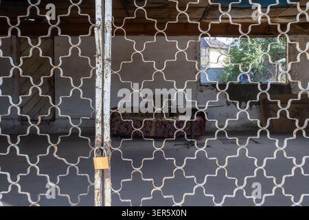 View through a decorative metal security grill into a cozy semi-outdoor Asian veranda (sit-out) with sofa and table. Typical South Asian residential a Stockfoto