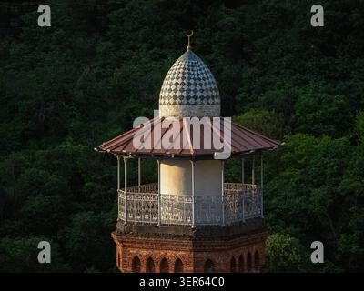 Juma ist eine Moschee in Tiflis im Bezirk Abanotubani. Goldener Halbmond glänzt auf der gewölbten Struktur. Gemusterte Fliesen reflektieren weiches Abendlicht. Dunkelgrünes Laub umrahmt die Szene. Eine ruhige Stille deutet auf leise Ehrfurcht hin. Ideal für spirituelle und kulturelle Zwecke Stockfoto