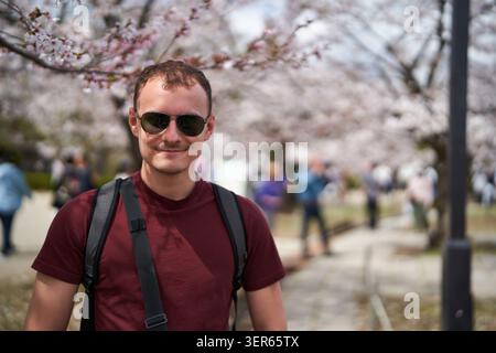 Junger Mann, der unter blühenden Kirschblüten in Japan lächelt Stockfoto