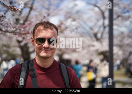 Junger Mann, der unter blühenden Kirschblüten in Japan lächelt Stockfoto