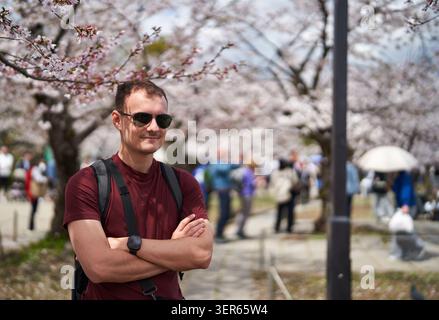 Junger Mann, der unter blühenden Kirschblüten in Japan lächelt Stockfoto