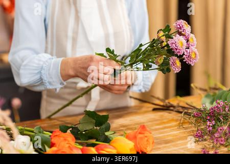 Blumenhändler, der rosafarbene Chrysanthemen für einen Blumenstrauß zubereitet, umgeben von bunten Blumen auf einem Holztisch in einem Blumenladen Stockfoto