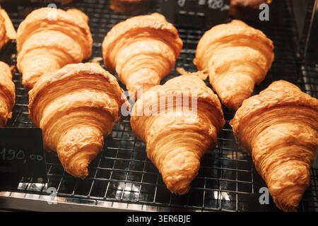 Gruppe frisch gebackener goldener Croissants auf einem Kühlregal aus Metall in einer Bäckerei, bereit zum Frühstück oder Snack Stockfoto