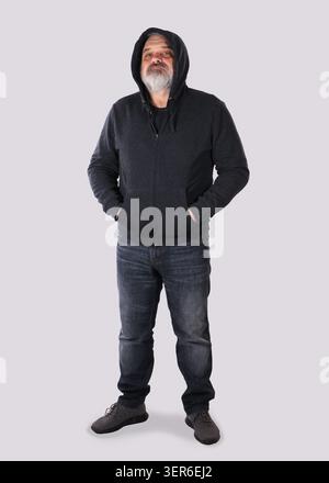Porträt eines Reifen bärtigen Mannes mit dunklem Hoodie und Jeans, der mit den Händen in den Taschen steht und nach oben blickt. Das Konzept des Vertrauens Stockfoto