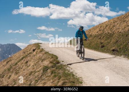 Mann in blauer Jacke und Helm, der ein E-Mountainbike auf einem gewundenen Feldweg auf einem grasbewachsenen Bergkamm fährt, Extremsportarten und Outdoor-Radfahren A Stockfoto