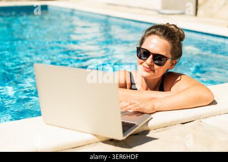Eine Frau trainiert in einem Schwimmbad mit einem Laptop. Stockfoto