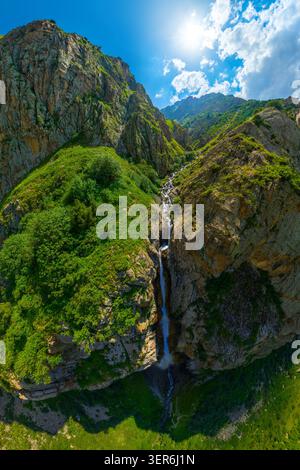 Der atemberaubende Bergwasserfall, der durch felsige Klippen in eine tiefe Schlucht stürzt, ist aus der Vogelperspektive zu sehen. Heller, sonniger Tag sorgt für lebhaftes Grün und klares W Stockfoto