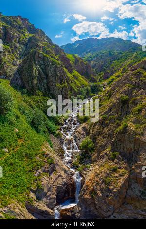 Aus der Vogelperspektive fängt das atemberaubende Bergtal mit einem kaskadierenden Wasserfall ein. Zerklüftete Berghänge, die mit grüner Vegetation bedeckt sind, verstärken die landschaftliche Schönheit. Stockfoto