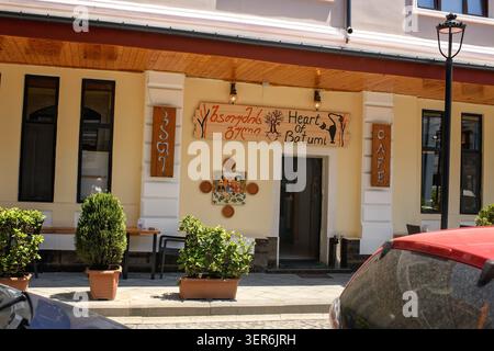 Batumi, Georgien - 09. Juni 2026: Gelbes Café mit rustikalem Holzschild mit georgianischer Schrift und ethnischer Kunst. Stockfoto