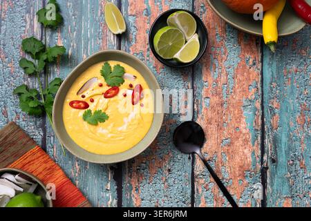 Kürbissuppe von oben, garniert mit Chili-Limette und Kräutern auf rustikal bemalten Holztisch Stockfoto