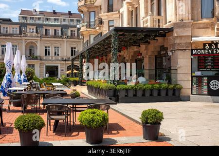 Batumi, Georgia - 9. Juni 2026: Lebhafte Restaurantterrasse in einer roten Backsteinstraße mit Gästen und Topfpflanzen. Stockfoto