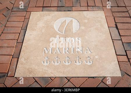 13. Mai 2026, Sigacik, Turkiye: Teos Marina Logo, Anker und Text in eine beige Steinplatte gehauen, umgeben von rötlichen Pflastersteinen Stockfoto