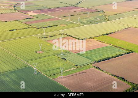Luftaufnahme mit einem Flickenteppich aus grünen und braunen landwirtschaftlichen Feldern mit Strommasten und Stromleitungen Stockfoto