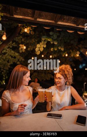 Freundinnen, die in der Bar im Freien Toast mit Bier machen Stockfoto