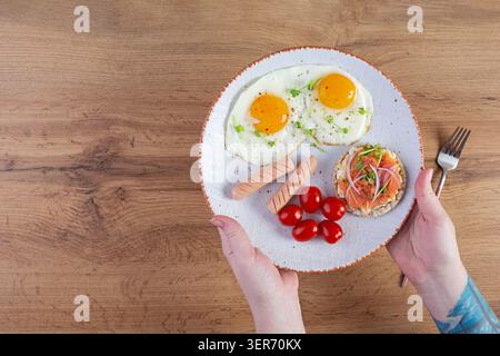 Spiegeleier mit Wurst, Kirschtomaten und Buchweizenbrot mit Lachsfisch. Mit den Händen im Rahmen Stockfoto