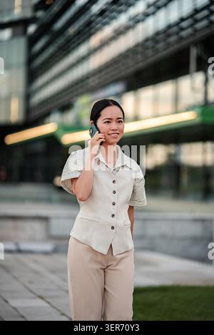 Asiatische Geschäftsfrau, die im Freien über Smartphone spricht, Karrierekommunikation Stockfoto