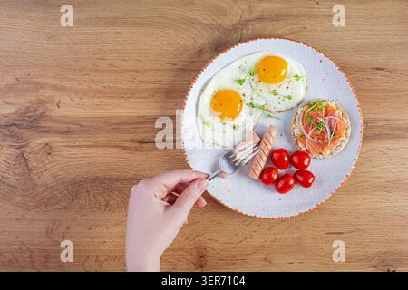 Spiegeleier mit Wurst, Kirschtomaten und Buchweizenbrot mit Lachsfisch. Mit den Händen im Rahmen Stockfoto