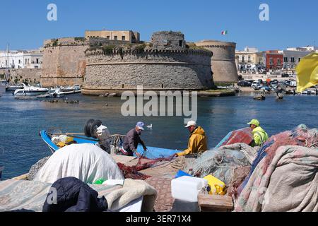 Italien, Region Apulien, Provinz Lecce: Gallipoli. Alte Fischer reparieren ihre Netze auf ihren bunten Booten, die am Fischerhafen angedockt sind. Hinter dem Ol Stockfoto