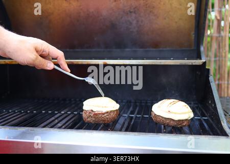 Nahaufnahme von Cheeseburgern, die auf einem heißen Grill kochen, perfekt für Partys im Hinterhof und Familientreffen. Stockfoto