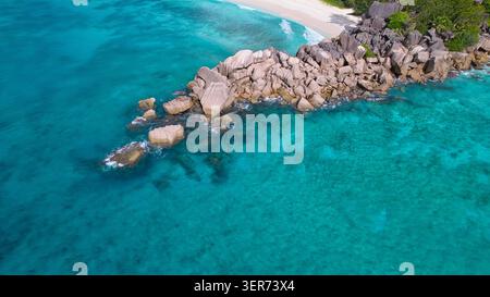 Atemberaubender Drohnenblick auf majestätische Granitfelsen, die das kristallklare türkisfarbene Wasser und den unberührten weißen Sand von Grand Anse und Petite Anse Beach trennen Stockfoto