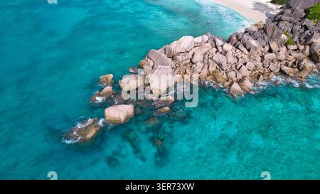 Atemberaubender Drohnenblick auf majestätische Granitfelsen, die das kristallklare türkisfarbene Wasser und den unberührten weißen Sand von Grand Anse und Petite Anse Beach trennen Stockfoto