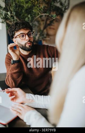 Junger Mann in Brille, der bei einem zwanglosen Geschäftstreffen Ideen mit Kollegen diskutiert Stockfoto