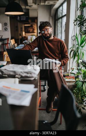 Junger Mann, der in einem Café auf einem Laptop arbeitet, während er geschäftlich telefoniert Stockfoto
