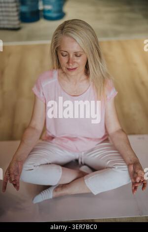 Reife Frau, die Meditation und Yoga praktiziert, sitzend im Kreuz auf einer Matte zu Hause Stockfoto