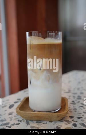 Kaffee in einem Glas mit Milch und Schaum auf dem Tisch Stockfoto