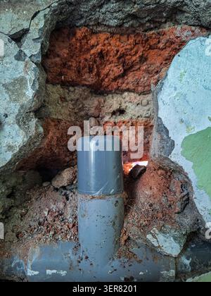 Nahaufnahme einer T-Verbindungskappe aus grauem Kunststoff-PVC-Sanitär in einer abgesprungenen Beton- und roten Tonziegelwand während der Renovierung des Badezimmers oder der Hausreparatur p Stockfoto