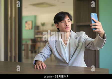 Authentisches horizontales Lifestyle-Porträt eines jungen, nicht binären thailändischen Isan-Profis oder Studenten, der ein Selfie oder Videoanruf macht. Eine Smar halten Stockfoto