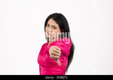 Unzufriedene junge Frau, die die Daumen nach unten zeigt und in die Kamera schaut Stockfoto