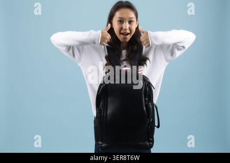 Fröhliche junge Frau mit schwarzem Rucksack auf den Schultern lächelnd Stockfoto