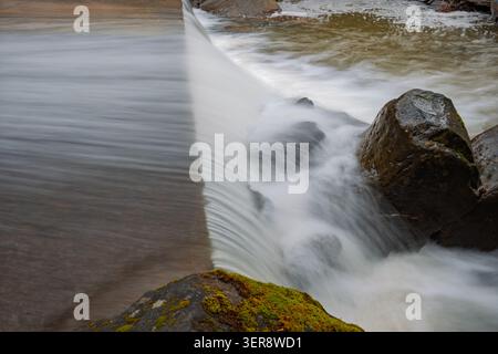 Seidenglattes Wasser fließt über Betonüberlauf Stockfoto