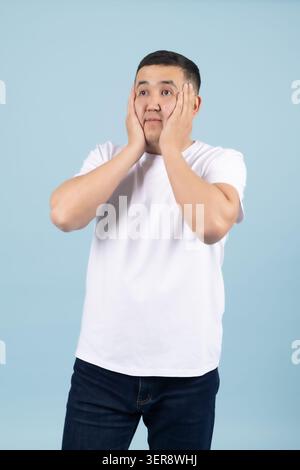 Ein wunderbarer junger, gutaussehender Mann, der in tiefem Unglauben Hände nahe seinem Gesicht hält Stockfoto