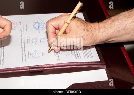 Die Hand einer Person, die einen Stift hält und ein amtliches rechtliches Dokument unterzeichnet Stockfoto