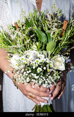 Frau mit einem schönen, rustikalen Hochzeitsstrauß mit weißen Blumen und grünen Kräutern Stockfoto