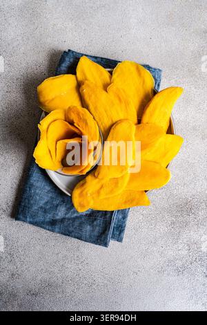 Ein Teller gefüllt mit leuchtenden gelben getrockneten Mangoblättern, elegant auf einem dunkelblauen Tuch angeordnet, bietet ein wunderbares Bild dieses süßen und gesunden Stockfoto