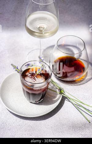 Erfrischender Eiskaffee, serviert in einem Glas mit Eiswürfeln, garniert mit Lavendel, neben einem weiteren Getränk in einem stilvollen Glas an einem Sommertag. Perfekt für Stockfoto