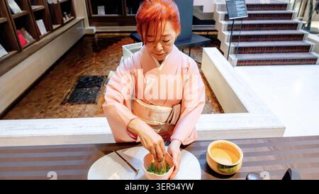 Japanische Frau im Kimono bereitet Matcha-Tee mit einem Bambusquirl zu, wobei der Schwerpunkt auf dem traditionellen japanischen Teezeremonie-Ritual an einem ruhigen Innentisch liegt Stockfoto