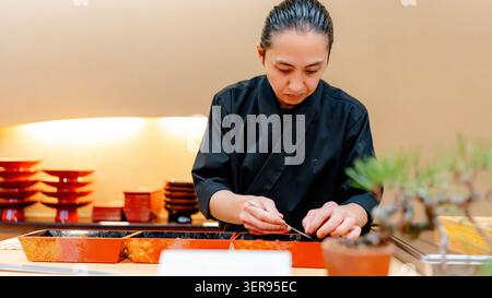 Der konzentrierte Sushi-Koch in traditioneller Kleidung bereitet Nigiri an einer minimalistischen Theke zu, in der japanische Kochkunst und Oakase-Dining-Atmosphäre präsentiert werden Stockfoto
