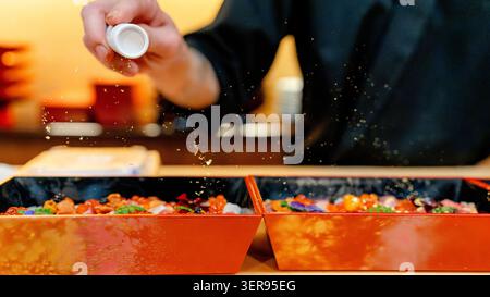 Nahaufnahme eines Küchenchefs, der in einem Restaurant in Tokio Chiriashi mit essbaren Goldflocken würzt und frischen Meeresfrüchten und Reis in lateinamerika und lateinamerika ein luxuriöses Funkeln verleiht Stockfoto