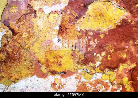 Nahaufnahme einer farbenfrohen, strukturierten Felsoberfläche mit natürlichen Rot- und Gelbtönen, die einem abstrakten Gemälde ähneln. Diese lebendige Mineralienpräsentation Stockfoto