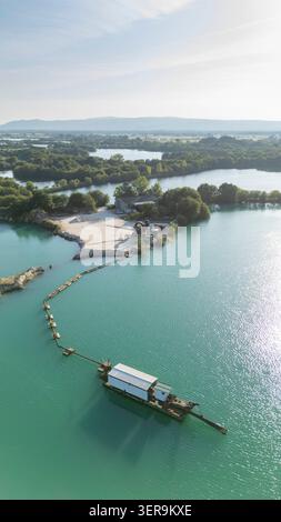 Aus der Vogelperspektive des Baggerbootes, das Sand aus einer Kiesgrube mit mehreren Seen in der Nähe einer Industrieanlage unter blauem Sommerhimmel extrahiert - Ourense, Spanien - Stockfoto