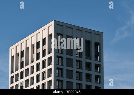 Modernes Apartmentgebäude mit geometrischer Fassade, Balkonen und Fenstern vor blauem Himmel für städtisches Wohnmotiv Stockfoto
