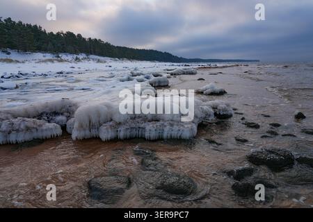 Gefrorene Ostseeküste mit eisbedeckten Felsen, Schnee und winterlichen Wellen in der Nähe der Klippen von Veczemju an der Vidzeme-Küste Lettlands. Stockfoto