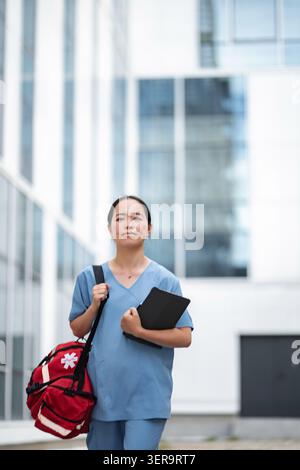 Weibliche Krankenschwester, die mit medizinischer Tasche und Tablette außerhalb des Krankenhauses geht Stockfoto